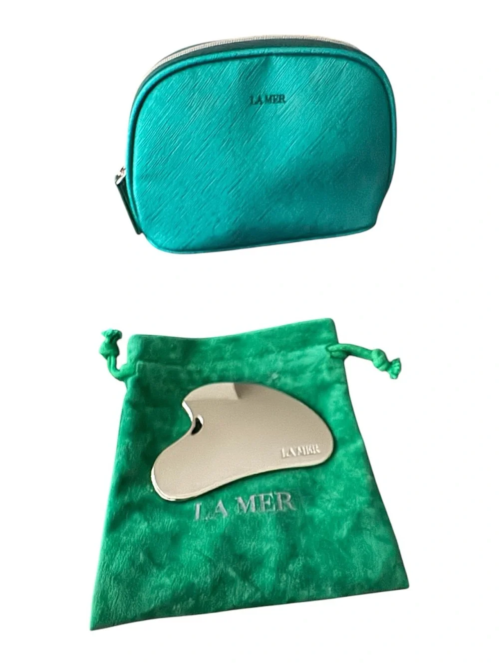 La Mer Silver Stainless Steel Gua Sha on Green Velvet Pouch and cosmetic bag